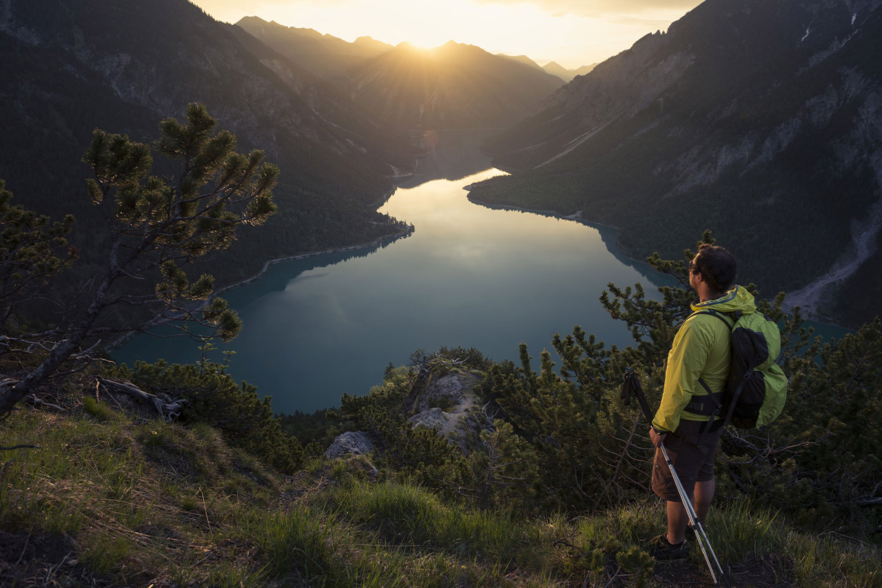 Ein Mann steht an einem Berghang und betrachtet den Sonnenaufgang.