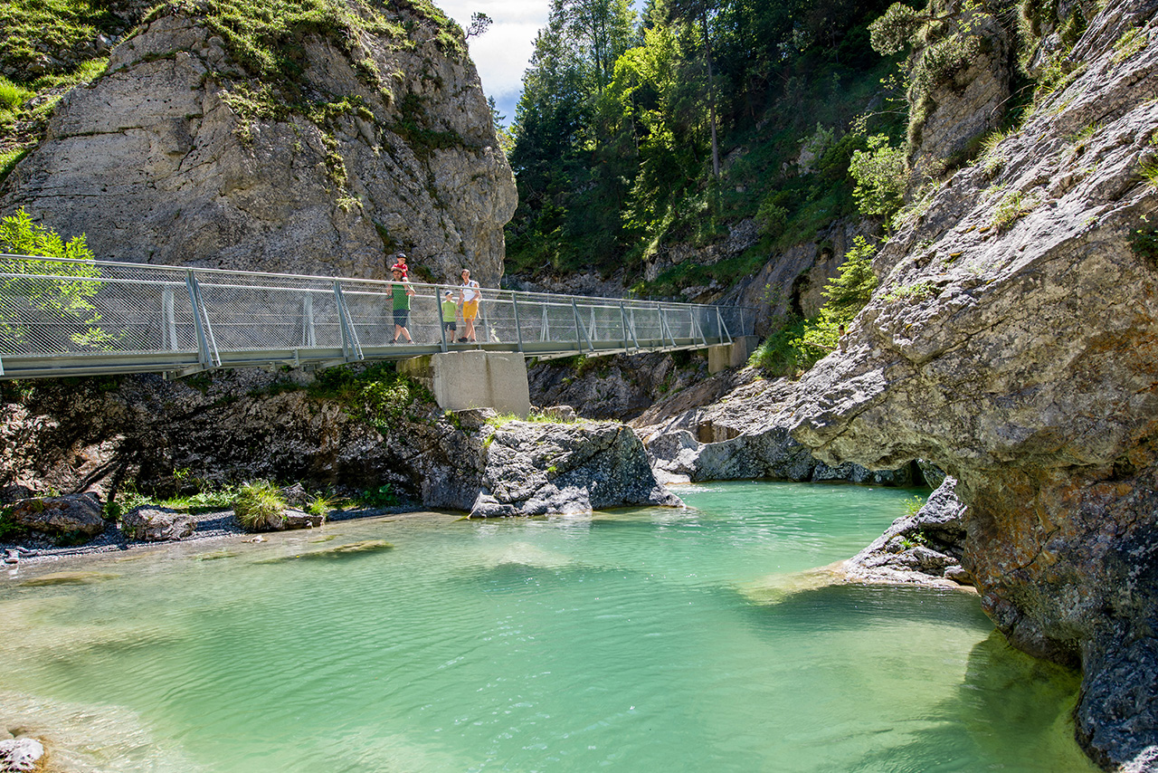  Die Stuibenfälle. Eine Brücke, die an einem Fels entlang geht. Unter der Brücke fließt ein Fluss.